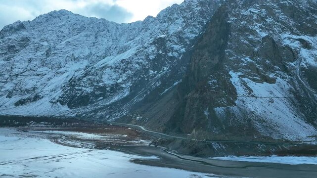 Drone pan shot of cliffs of snowy mountains and roads passing by it in Skardu, Pakistan.