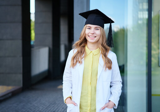 Young blond female in medical uniform and graduation cap looking at the camera and smiling. Standing outside, happy to finish studying in healthcare or veterinary. High quality photo