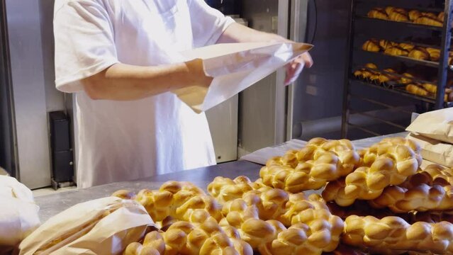 A bakery worker packs rolls into paper bags. the baker prepares orders for customers with rolls and whole dough products. Work process in a bakery with dough products. Successful family business