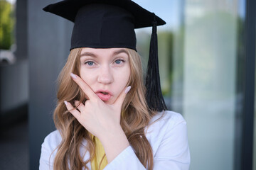 Young blond female in medical uniform and graduation cap with funny emotions and in a good mood. Standing outside, happy to finish studying in healthcare or veterinary. High quality photo