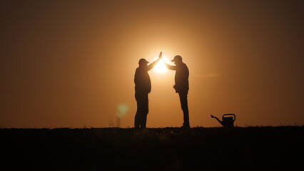Fototapeta premium Silhouettes of two successful farmers in a field making a high five gesture