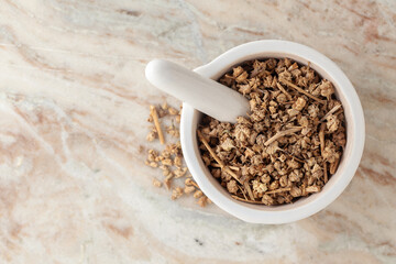 Top-view of Dry Organic Gokhuru (Tribulus terrestris) fruits, in white ceramic mortar and pestle, on a marble background.