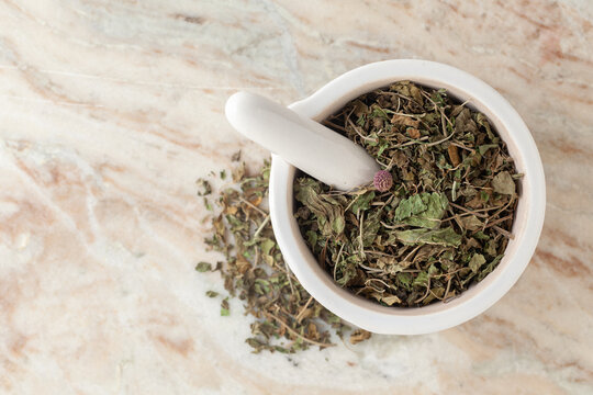 Top-view of Dry Organic Gymnema or Gurmar (Gymnema sylvestre) leaves, in white ceramic mortar and pestle, on a marble background.