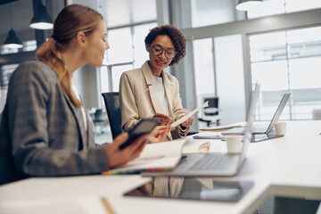 Young female colleagues using gadgets while working together in modern coworking indoors