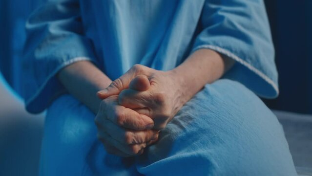 Close-up of hands of worried unrecognizable Caucasian female patient in blue medical gown getting ready for undergoing diagnostic procedure in hospital