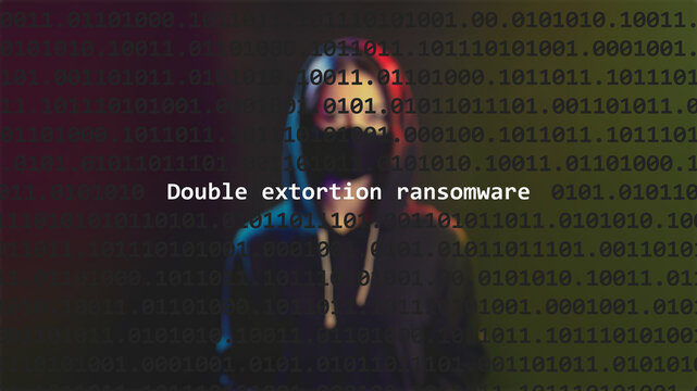 Cyber attack double extortion ransomware text in foreground screen, anonymous hacker hidden with hoodie in the blurred background. Vulnerability text in binary system code on editor program.