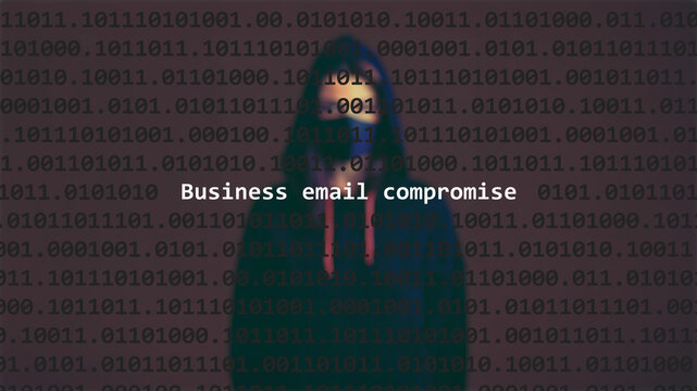 Cyber attack business email compromise text in foreground screen, anonymous hacker hidden with hoodie in the blurred background. Vulnerability text in binary system code on editor program.