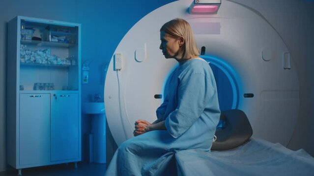Medium slowmo shot of anxious mature Caucasian female patient sitting in medical examination room before undergoing magnetic resonance imaging in diagnostic clinic