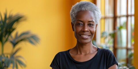Obraz premium Smiling mature woman with grey hair standing against a yellow background, with plants in the background.