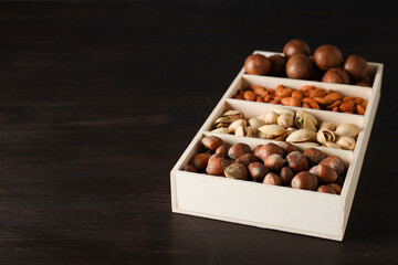 Wooden box with different nuts on a dark background