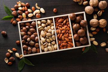 Wooden box with different nuts on a dark background