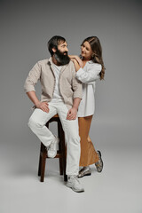 A man and woman dressed in sophisticated attire pose together against a grey backdrop.