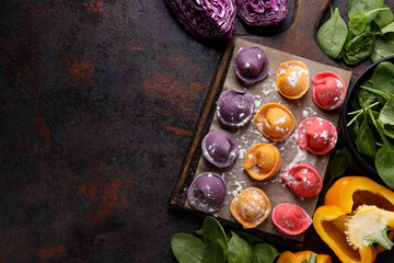 Colored dumplings on board and vegetables on dark background, space for text