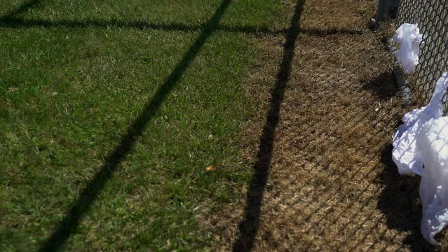 Empty baseball diamond with litter and trash stuck to a fence on a hot summer day