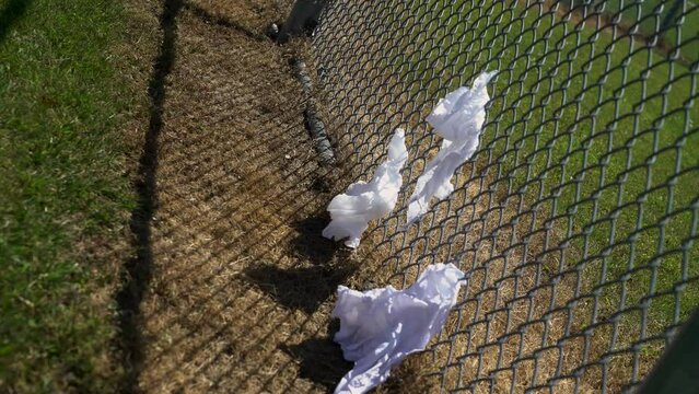 Empty baseball diamond with litter and trash stuck to a fence on a hot summer day