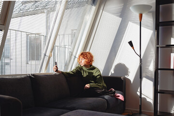 young red-haired woman in living room on sofa using phone