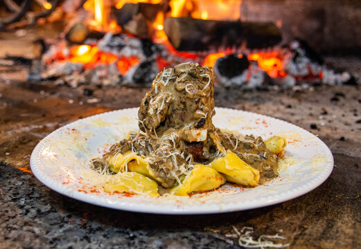 White plate with meat, cheese, tortelone and sauce and grated cheese on top. Delicious plate of food in front of the fire.