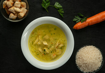 Chicken soup with rice and carrots on a black background, top view