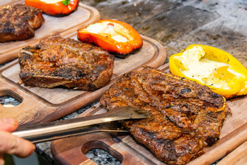 Chef's hand putting a big piece of grilled meat on a wooden board, with a piece of pepper with cheese on the side. 