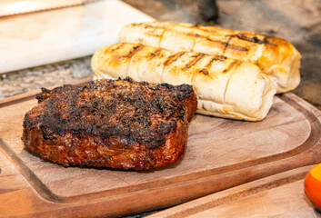 Wooden board with big piece of grilled meat and garlic bread.