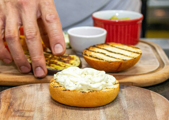 Chef hands starting the preparation of a vegetarian hamburger with bread, eggplant and sausage. Burger prepared on a restaurant kitchen. Professional chef is preparing burger. Burger making.