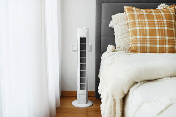 White tower fan next to the bed in a modern bright bedroom