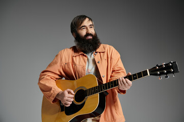 Obraz premium A man with a beard plays an acoustic guitar in a studio with a grey background.
