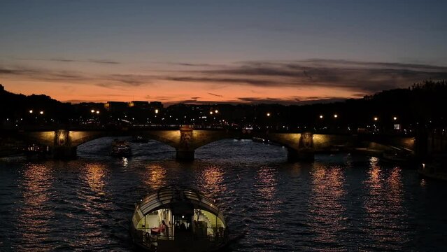 A riverboat sails down the Seine River in the centre of Paris against a backdrop of bridges at sunset