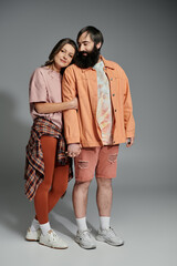 A loving couple, dressed in casual peach-toned outfits, pose affectionately against a grey backdrop.