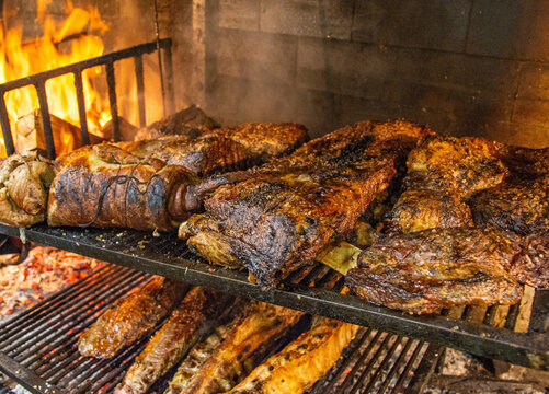 Various types of meat being roasted in a typical Uruguayan grill called parrilla supplied with firewood and flames in a restaurant kitchen.