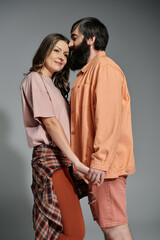 A couple in sophisticated attire poses together against a gray background.