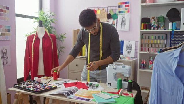 African american male tailor using measuring tape in a colorful atelier with mannequin and sewing machine