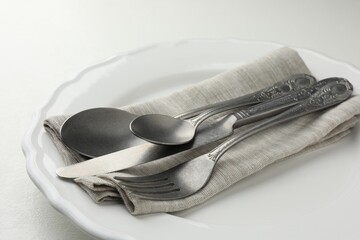 Stylish setting with cutlery, napkin and plate on white table, closeup