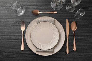 Stylish setting with cutlery, glasses and plates on black wooden table, flat lay