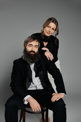 A loving couple in sophisticated attire pose together in a studio setting.