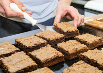 Chef's hands cutting pieces of freshly made brownie with a spatula in restaurant kitchen.