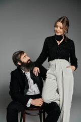 A loving couple, dressed in sophisticated attire, pose together against a gray backdrop.
