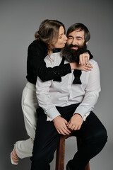 A stylish couple poses together, the woman leaning in to kiss the man on the cheek.