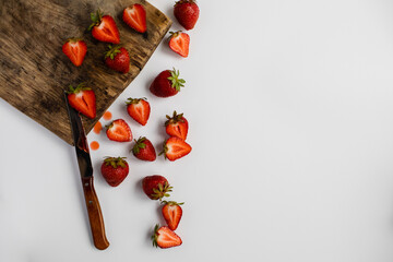 A top view of the cut ripe strawberries on a brown, wooden board. Free space for text on a white background
