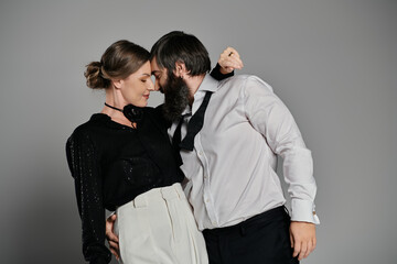 A loving couple, dressed in sophisticated outfits, pose together against a gray backdrop.