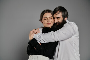 A loving couple in sophisticated attire poses for a portrait, embracing each other with tenderness.