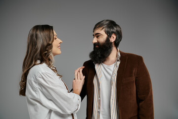 A couple in sophisticated attire stands closely, the woman gently resting her hand on the mans shoulder.