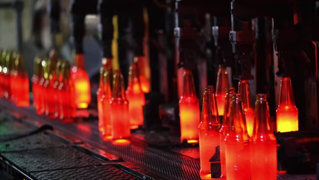 Glass factory, production of glass containers. Molten glass is blown into molds. Robotics in industry. Modern technologies, robotic machines produce products. Technological work at the plant.