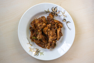 Delicious Irani chicken kadai bhuna curry on a white plate on wooden background. Tasty Iranian chicken kadhai recipe. Top view.