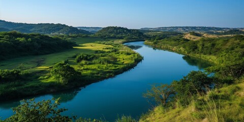 Fototapeta premium A breathtaking landscape capturing a meandering river amidst vibrant green hills under a clear sky