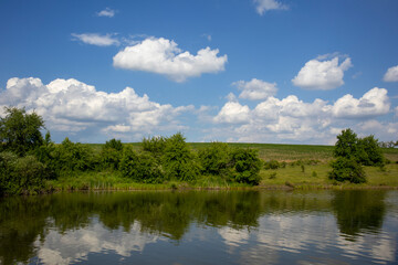 Tranquil scenery with a lake reflecting the blue sky and white clouds on a sunny day
