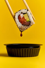 A sushi roll is dipped in soy sauce and a drop flows from it.