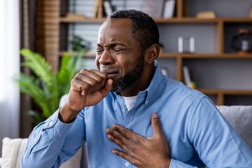 Man clutching chest and coughing, depicting symptoms of illness or respiratory distress in a home...