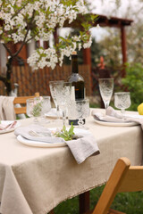 Stylish table setting with beautiful spring flowers, wine, plates and glasses in garden
