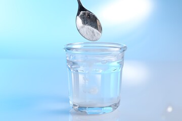 Adding baking soda into glass of water on light blue background